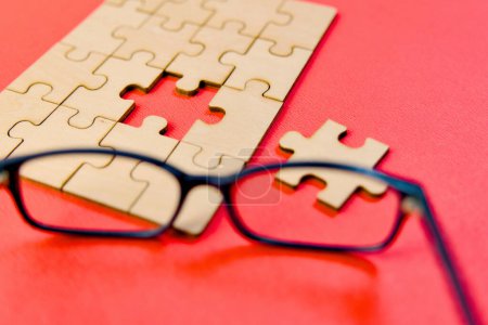 This image depicts a pair of eyeglasses resting beside a partially completed jigsaw puzzle on a red surface