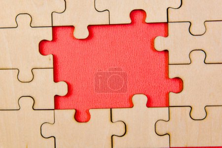 A close-up view of unfinished wooden puzzle pieces scattered across a vibrant red background