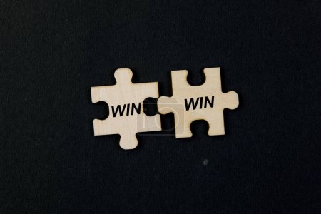 Nahaufnahme zweier Puzzleteile, die zusammenpassen, um den Text "Win Win" auf schwarzem Hintergrund zu erzeugen