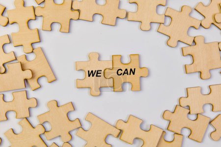 A close-up image of unfinished wooden jigsaw puzzle pieces interlocking to create the phrase "We Can,"
