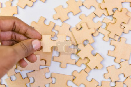 Close up of human hand putting jigsaw puzzle piece on white background