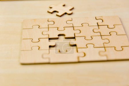 A close-up photo of unfinished wooden puzzle pieces scattered on a smooth wooden table