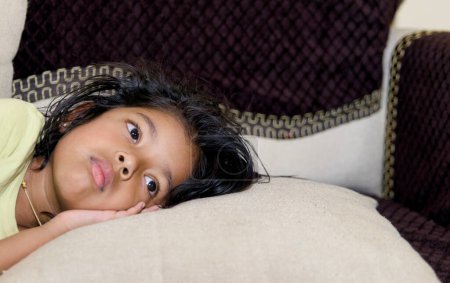 This image is about little asian girl sadly lying on the sofa in the living room at home