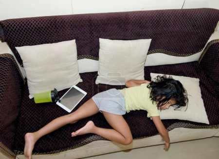 Ein junges Mädchen liegt bequem auf einer Couch, in ein digitales Tablet vertieft.