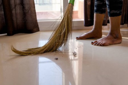 A focused woman sweeps the floor with a broom, keeping her living space clean and organized.