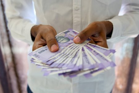 Gros plan des mains de l'homme d'affaires comptant méticuleusement des piles de billets de 100 roupies sur un bureau propre et organisé dans un bureau moderne.