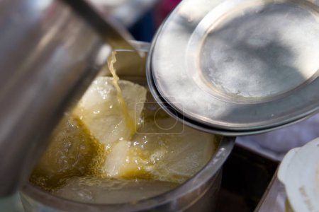Ein Verkäufer gießt Zuckerrohrsaft in ein mit Eiswürfeln gefülltes Glas, wodurch ein kühles und erfrischendes Getränk entsteht, das perfekt für einen heißen Sommertag ist.