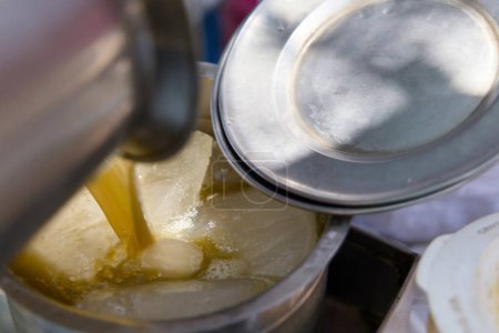 Ein Verkäufer gießt Zuckerrohrsaft in ein mit Eiswürfeln gefülltes Glas, wodurch ein kühles und erfrischendes Getränk entsteht, das perfekt für einen heißen Sommertag ist..