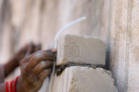 A close-up view of a construction worker carefully checking the alignment of a concrete block on a wall with a level tool