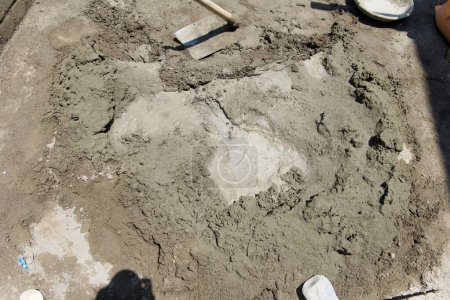 A close-up view of a construction site reveals essential building materials a well-used shovel, a pile of sand, and several sacks of cement sitting on a concrete surface.