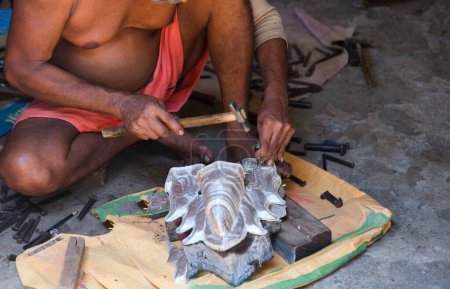 A skilled Indian craftsman meticulously works on a metal form to create a statue of a Hindu god