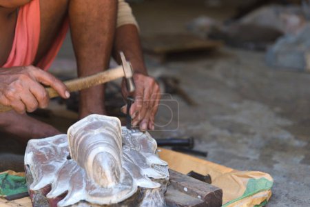A skilled Indian craftsman shaping metal to create a religious idol in his workshop.