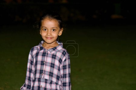 A young little girl with a big smile on her face stands in a park at night