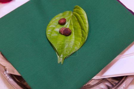Nahaufnahme eines Betelblattes mit ein paar Betelnüssen, die auf einem luxuriösen smaragdgrünen Saree ruhen