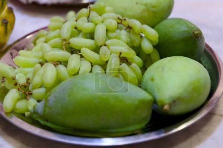 This image is about Green mangoes and grapes on a metal plate Selective focus