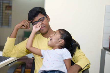 Ein engagierter indischer Vater, der in seinem Homeoffice an einem Laptop arbeitet, nimmt sich einen Moment Zeit, um sich mit seiner verspielten Tochter zu verbinden.