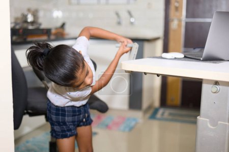 A young girl independently adjusts the height of her laptop computer stand while working in a bright, sunny kitchen.