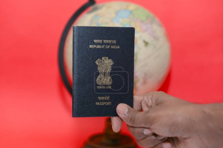This image is about Man hand holding Indian passport and globe on red background Travel concept