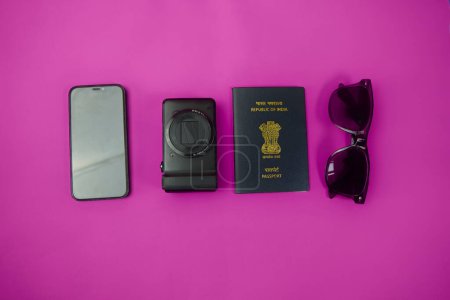 Pasaporte indio, gafas de sol aviador, y un teléfono inteligente moderno arreglado sobre un fondo rosa vibrante. Perfecto para conceptos de viaje