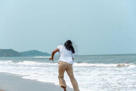 Eine fröhliche Frau sprintet an einem sonnigen Strandtag auf das Meer zu und fängt die Essenz unbeschwerter Strandabenteuer ein