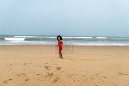 Un petit se dresse sur une vaste plage de sable, regardant les vagues ondulantes de l'océan