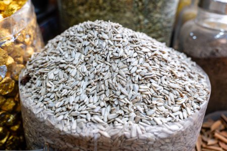 A close-up view of a heap of fresh sunflower seeds in a transparent container at a bustling market stall.
