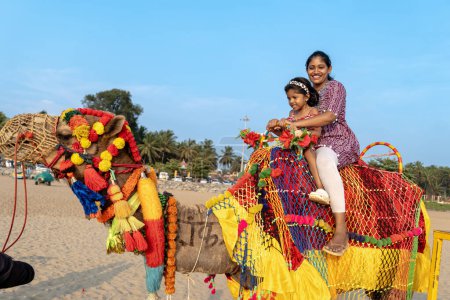 A sun-kissed beach ride on a vibrant camel brings joy to a mother and her daughter.