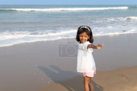 Ein kleines Kind steht am sandigen Ufer und streckt sich den Meereswellen entgegen. Unschuld und Erforschung treffen in diesem heiteren Strandmoment aufeinander.