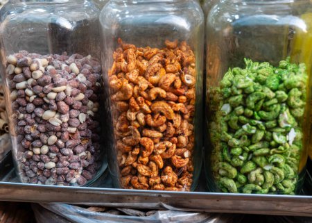 Three glass jars brim with an assortment of masala nuts purple speckled richly coated brown and vibrant green A flavourful display for food related stock images