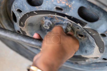 Gros plan des mains retirant les écrous de roue d'un pneu de voiture pendant l'entretien.