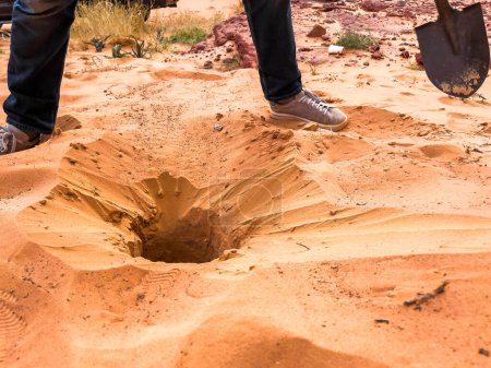 Mann gräbt mit Schaufel ein Loch in der Wüste