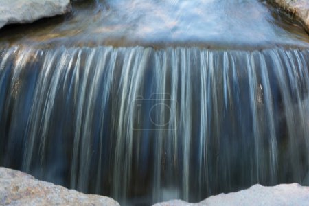 Photo for The photo depicts a streambed with water falling from a small height. The photo was taken with a long exposure, so the water is beautifully blurred, and only fragments of stones at the bottom are visible. - Royalty Free Image