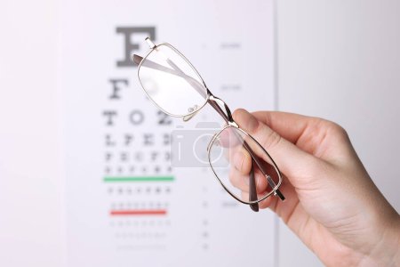 Photo for Vision correction glasses in hand against the background of a vision test table with space for text. High quality photo - Royalty Free Image