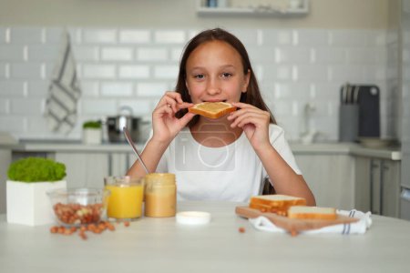 Foto de Una chica de buen humor haciendo un sándwich de mantequilla de maní en la cocina. Foto de alta calidad - Imagen libre de derechos