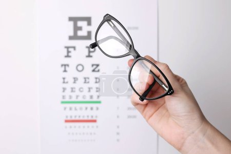 Photo for Vision correction glasses in hand against the background of a vision test table with space for text. High quality photo - Royalty Free Image