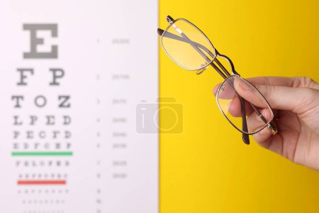 Téléchargez les photos : Lunettes de correction de la vue en main sur le fond d'une table de test de vision avec espace pour le texte. Photo de haute qualité - en image libre de droit