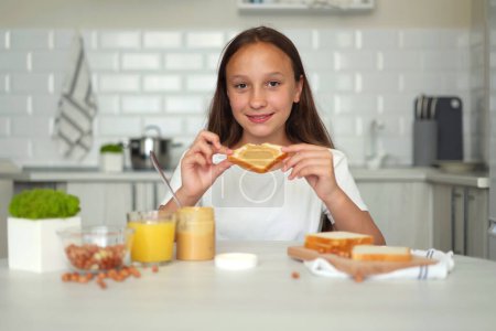 Photo for A girl in a good mood making a peanut butter sandwich in the kitchen. High quality photo - Royalty Free Image