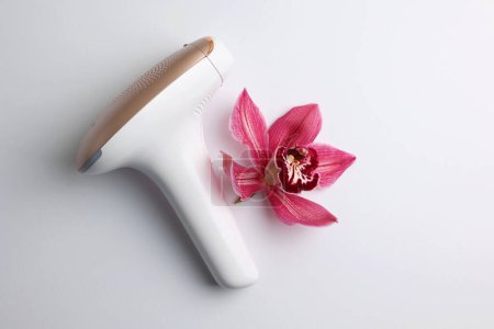 Photo for A hair removal device next to a pink flower with delicate petals on a white surface, creating a beautiful contrast of colors and textures - Royalty Free Image