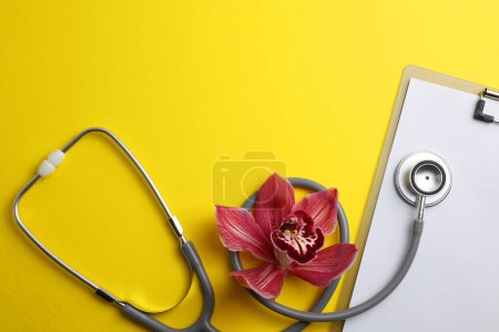 Photo for Orchid and stethoscope on a colored background, top view. Symbol of womens health and gynecology. High quality photo - Royalty Free Image
