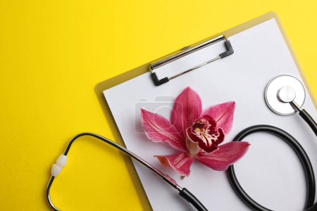 Foto de Orquídea y estetoscopio sobre un fondo de color, vista superior. Símbolo de la salud y la ginecología de las mujeres. Foto de alta calidad - Imagen libre de derechos
