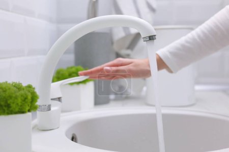 Téléchargez les photos : Une fille ouvre l'eau du robinet dans la cuisine dans un intérieur moderne. Eau purifiée, hygiène. Photo de haute qualité - en image libre de droit
