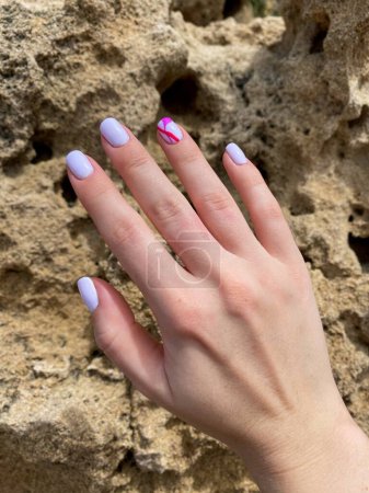 Ongles féminins avec une belle manucure rose clair sur un fond de grottes, ongles de forme carrée. Photo de haute qualité