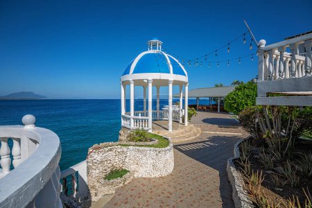 Foto de Sosua, República Dominicana - 10 de marzo de 2024: Hermosa vista al territorio del Piergiorgio Palace Hotel con mirador blanco y jardín de flores tropicales en el fondo del océano Atlántico. - Imagen libre de derechos