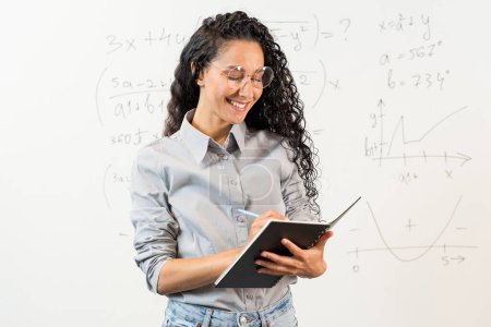 Porträt einer jungen nachdenklichen orientalischen Studentin, die auf dem Campus der modernen Bürouniversität auf Notizbuch schaut, Notizen macht, Projektstrategie. Lockiger arabischer Student mit Brille