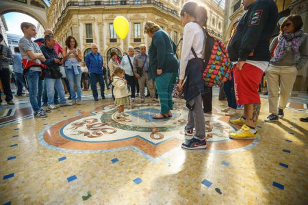 Foto de MILÁN, ITALIA - 2 DE OCTUBRE DE 2015: Los turistas rodean tres veces en el suelo los testículos de un toro de mosaico, se cree que trae suerte a la persona, en la Galería Vittorio Emanuele, en Milán - Imagen libre de derechos