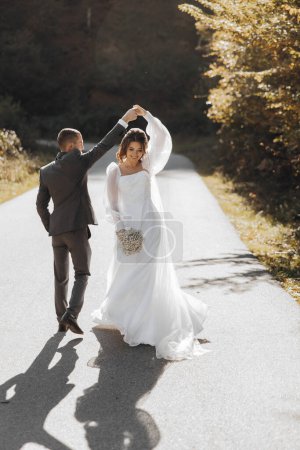 Téléchargez les photos : Le marié tourne la mariée sous son bras. heureux le voile flotte dans le vent. Couple doux et élégant. - en image libre de droit