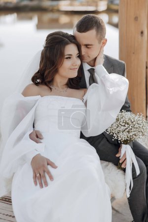 Photo for A beautiful young girl on a swing with her groom. She romantically leaned against him. He kisses her in a beautiful soft light. - Royalty Free Image