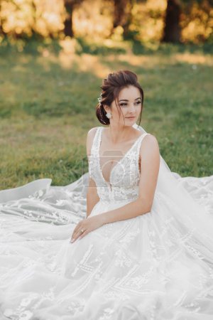 Photo for Wedding portrait of the bride. A beautiful bride is sitting in a white dress on green grass. Green background. Beautiful makeup. A young girl. Summer - Royalty Free Image