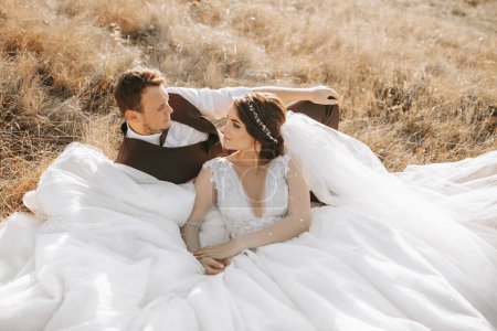 portrait of a stylish groom with a bride on a background of autumn dry grass. the concept of a rural wedding in the mountains, happy bohemian newlyweds. the bride and groom are lying on the grass