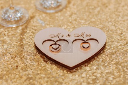 Téléchargez les photos : Anneaux de mariage sur un support en bois debout sur une table recouverte d'or - en image libre de droit